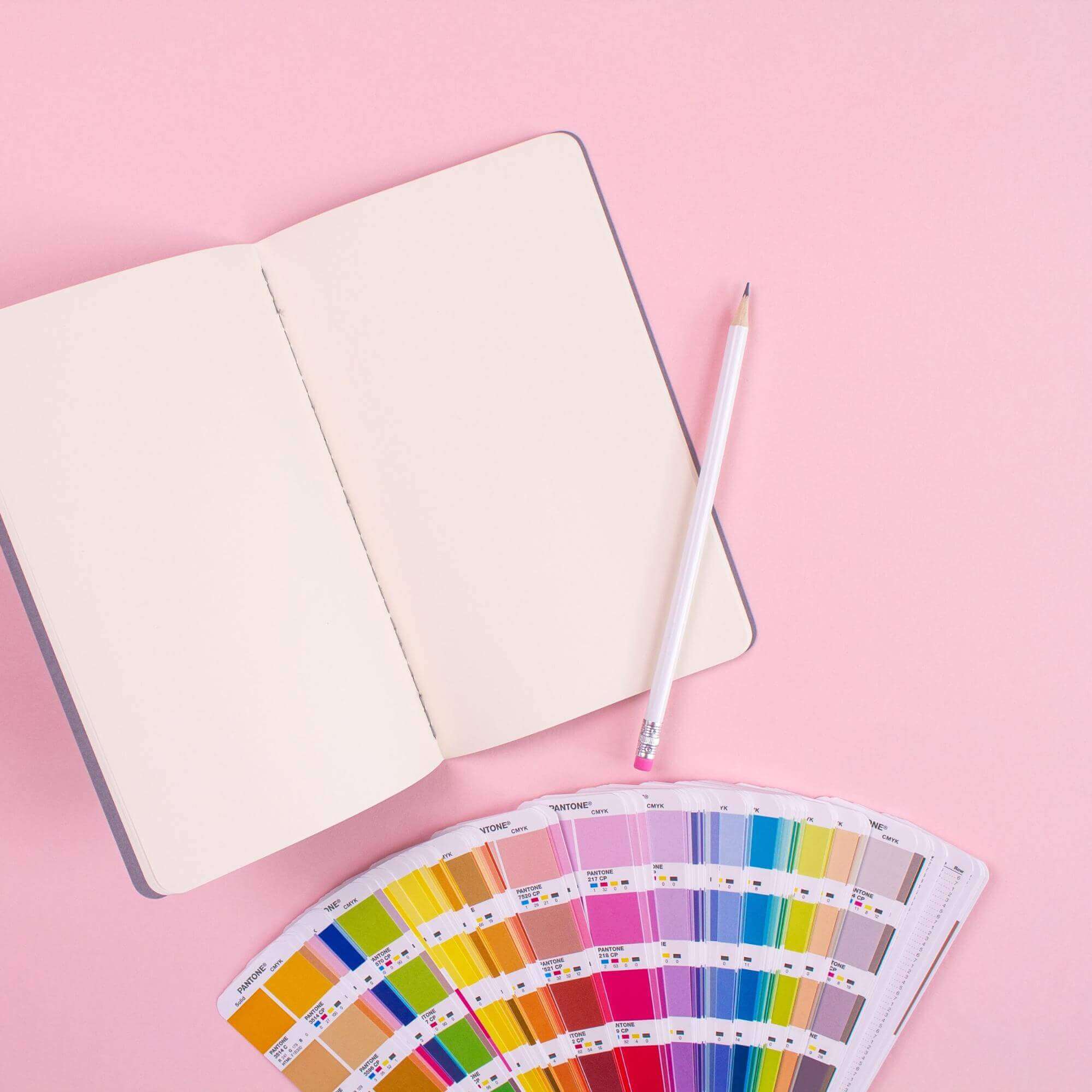 a photo of a notebook, a pencil and a color palette, indicating a design process.